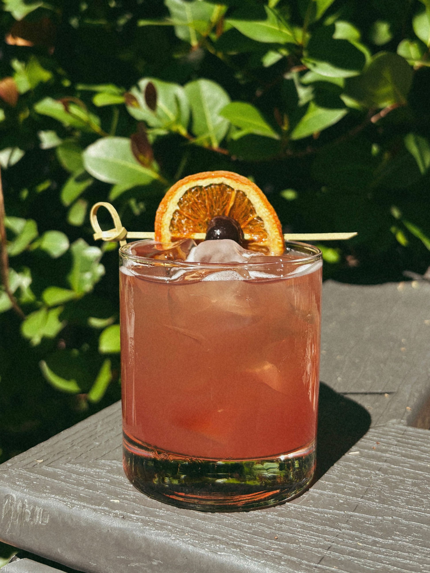 Bourbon smash cocktail with dried orange garnish and cherry, served outdoors