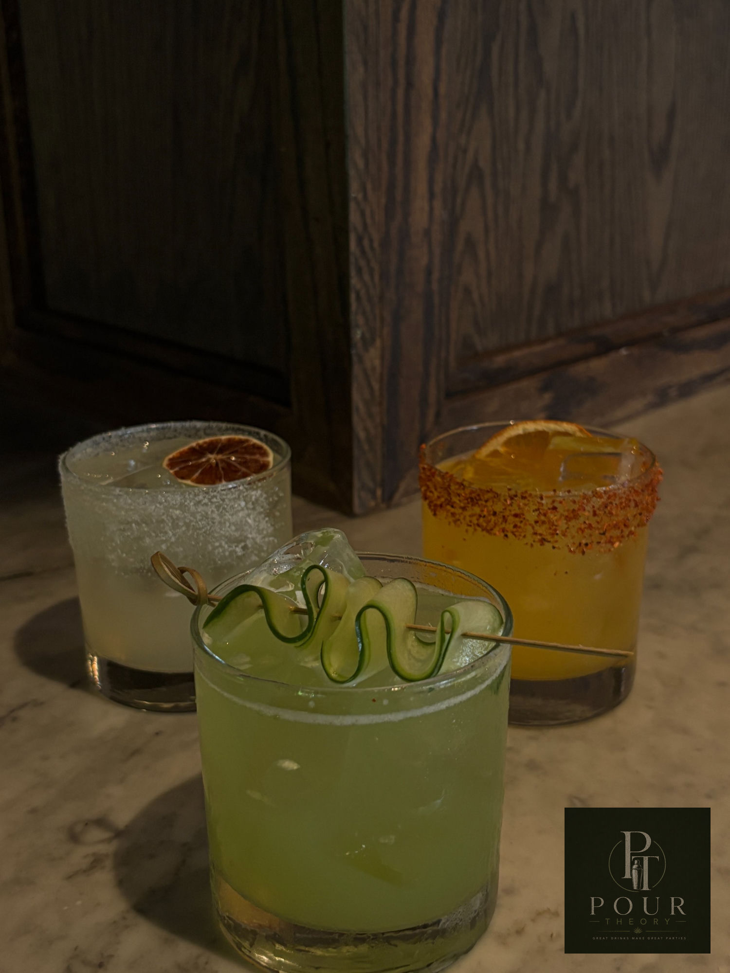 Three signature craft cocktails lined up on marble — cucumber margarita, mezcal sour, and spicy mango